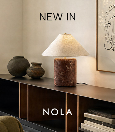 Nola table lamp with a reddish-brown marble base and a conical linen shade on a dark sideboard. Text: ‘New In – Nola’.