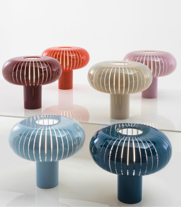 Six decorative table lamps from Kartell in different colours with a ribbed, mushroom-shaped design on a reflective surface.