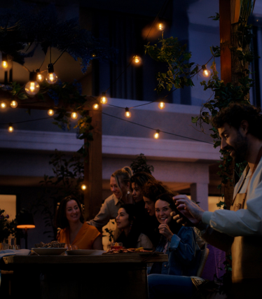 Modern exterior wall with two Aludra Double wall lights from Nordlux. The lights shine their light upwards and downwards, creating an elegant, warm play of light on the bright façade. In front of the house, green ornamental grasses and clean lines create a stylish, architectural ambience.