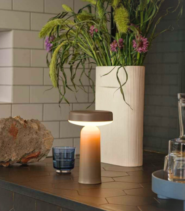Portable Ease table lamp by Muuto on a dark kitchen worktop with floral decoration.