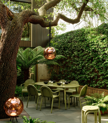 Tom Dixon outdoor lamps in a stylish garden with a dining area beneath an old tree.