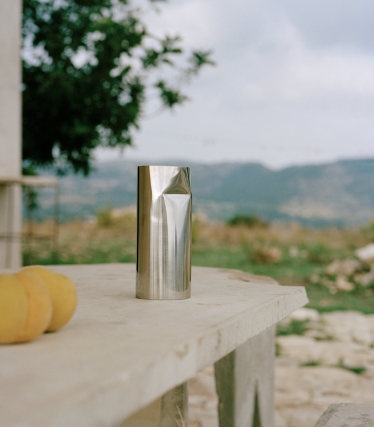 Brushed metal cup on stone slab outdoors, soft landscape in the background.