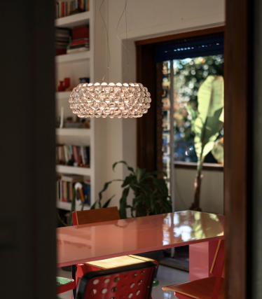 Spherical pendant light made of glass globes above a red dining table, viewed through a doorway.