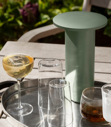 Sage green cylindrical side table/cooler on a tray with glasses and drinks outdoors..