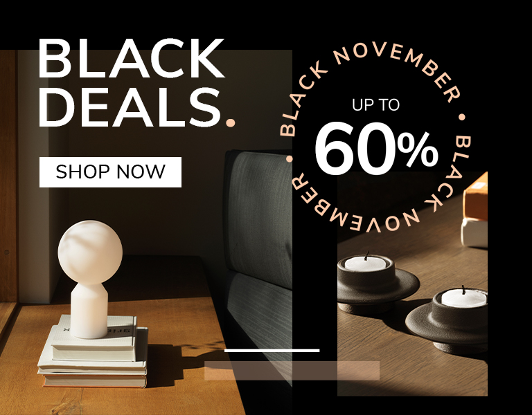Modern interior scene with a small sculptural table lamp on stacked books and minimalist candle holders on a wooden table, promoting Black November deals with up to 60% off.